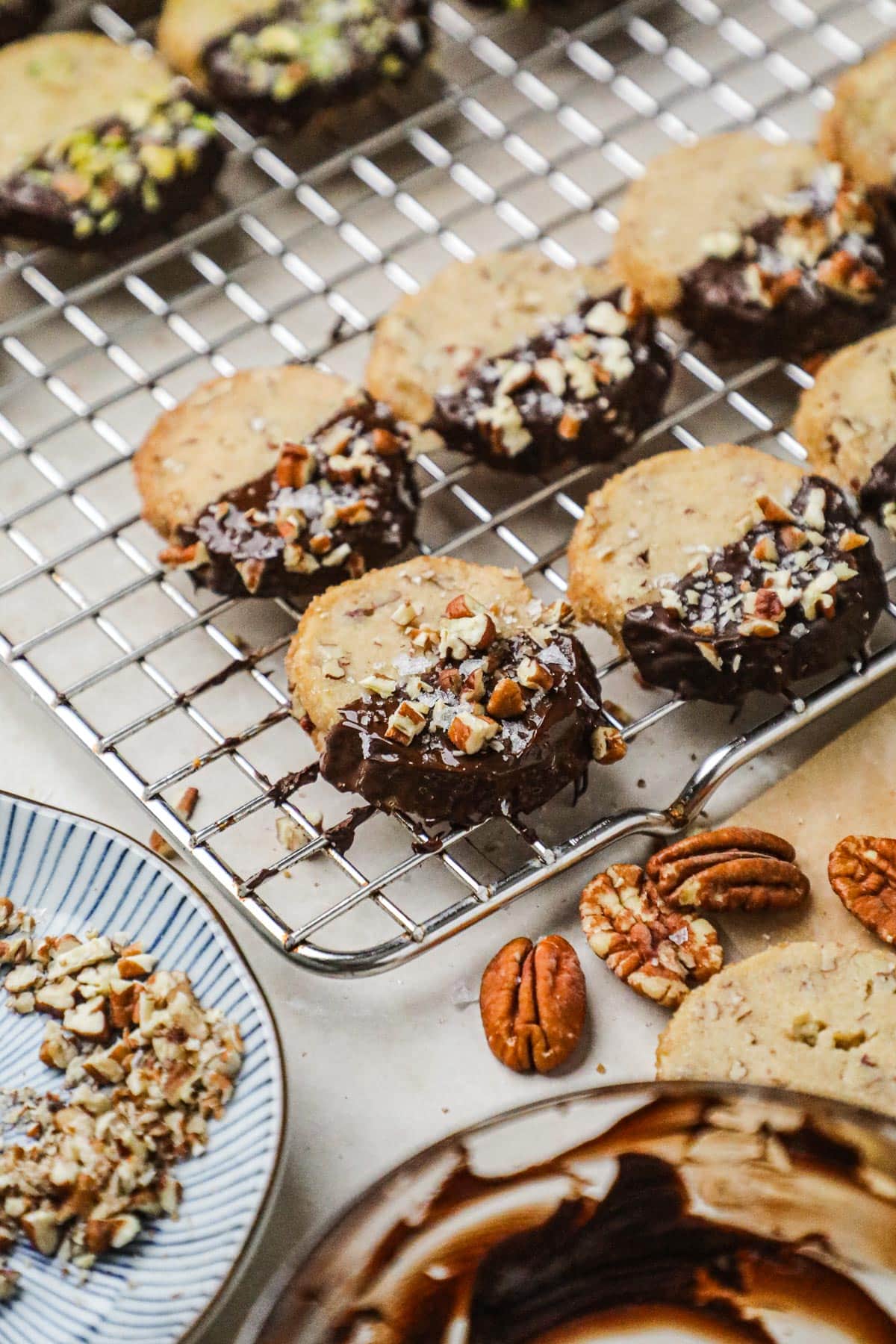 Chocolate-dipped brown sugar shortbread with chopped pecans and flaky sea salt drying on a wire cooling rack.