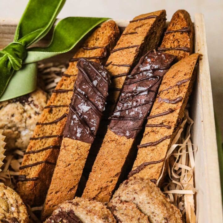 Dark chocolate-dipped espresso brown butter biscotti in a holiday cookie box with a green velvet ribbon.