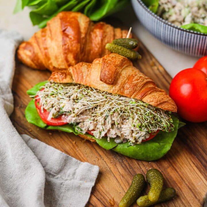 Tuna salad croissant sandwich with sprouts, tomato, lettuce, and cornichons.