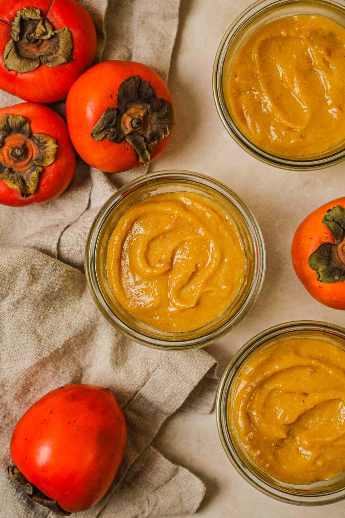 Homemade cinnamon persimmon curd in jars with ripe fuyu and hachiya persimmons.