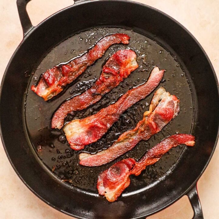 Bacon cooked in a cast iron skillet on a stovetop.