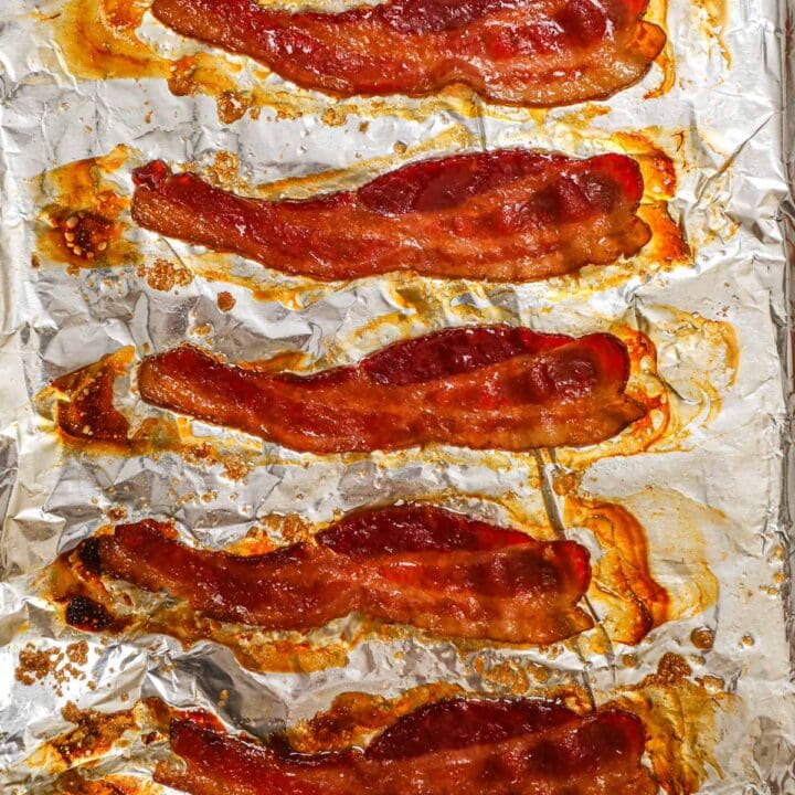 Oven-baked brown sugar bacon with caramelized edges on a baking sheet.