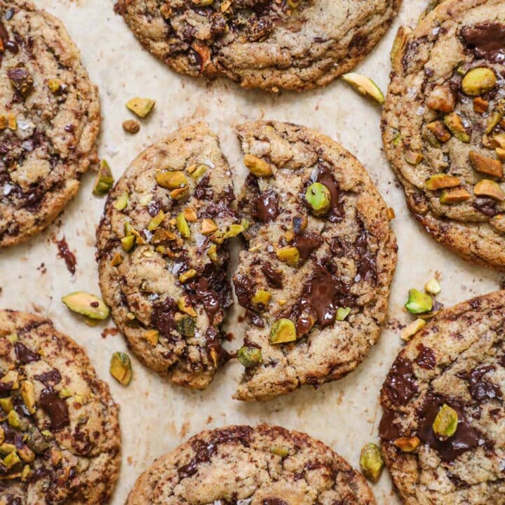 Brown butter pistachio chocolate chip cookies with flaky sea salt on a parchment paper-lined baking sheet.