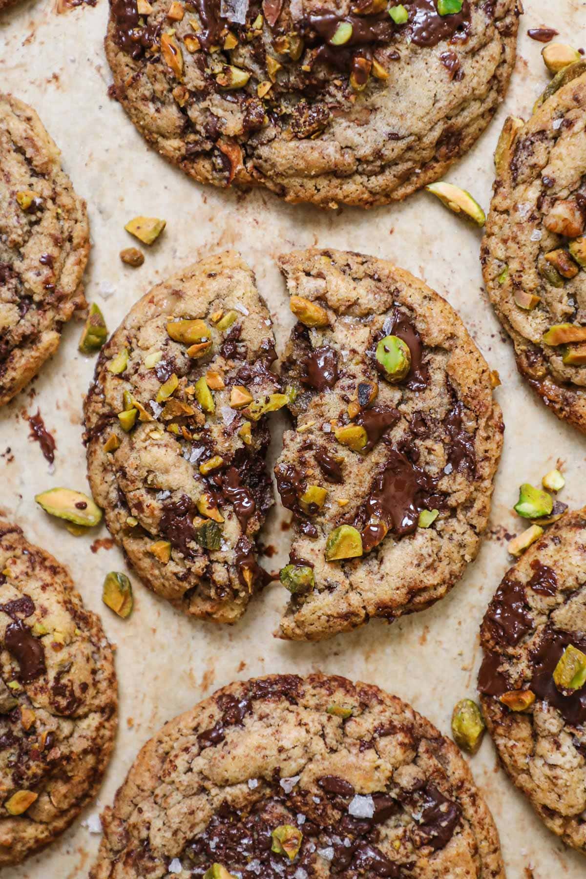 Brown butter pistachio chocolate chip cookies with flaky sea salt on a parchment paper-lined baking sheet.